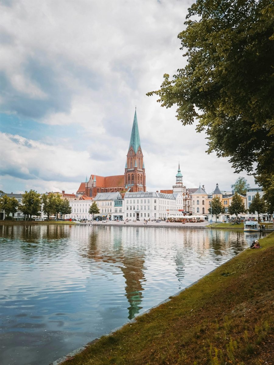 Scenic view of Schwerin's skyline reflecting in Pfaffenteich pond, showcasing iconic towers and urban charm.